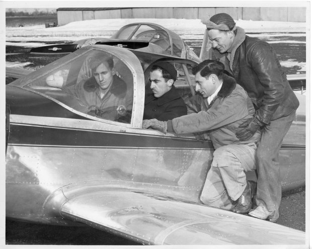 Tony Riccio and three unknown people look at a Globe Swift's cockpit and instrument panel.